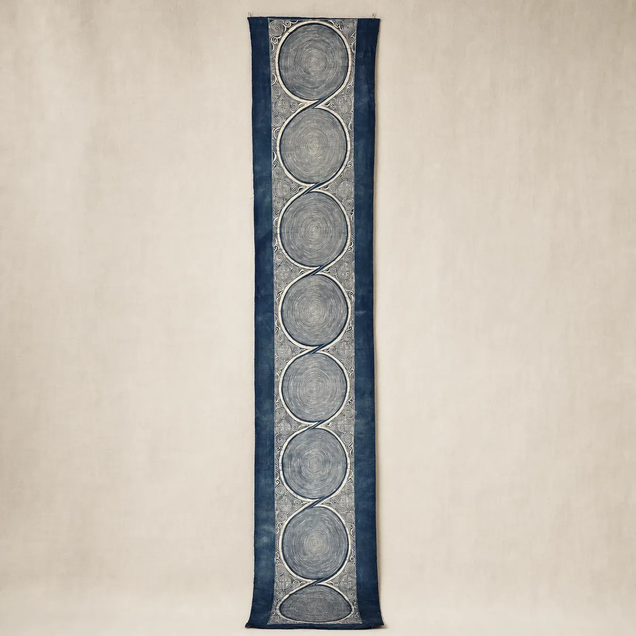 Full-length indigo Wotuo spiral cotton batik textile on a warm ivory backdrop