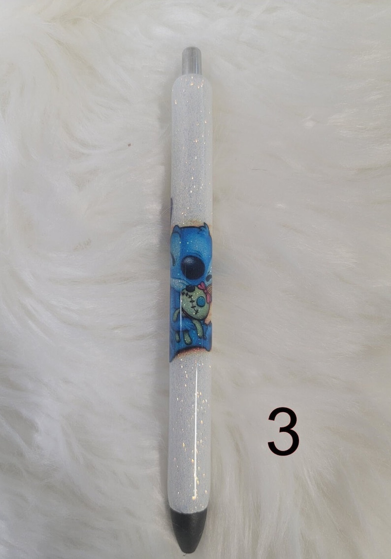 May include: A white glitter pen with a blue cartoon character holding a doll. The character is on the pen's barrel. The number 3 is in the bottom right corner of the image.