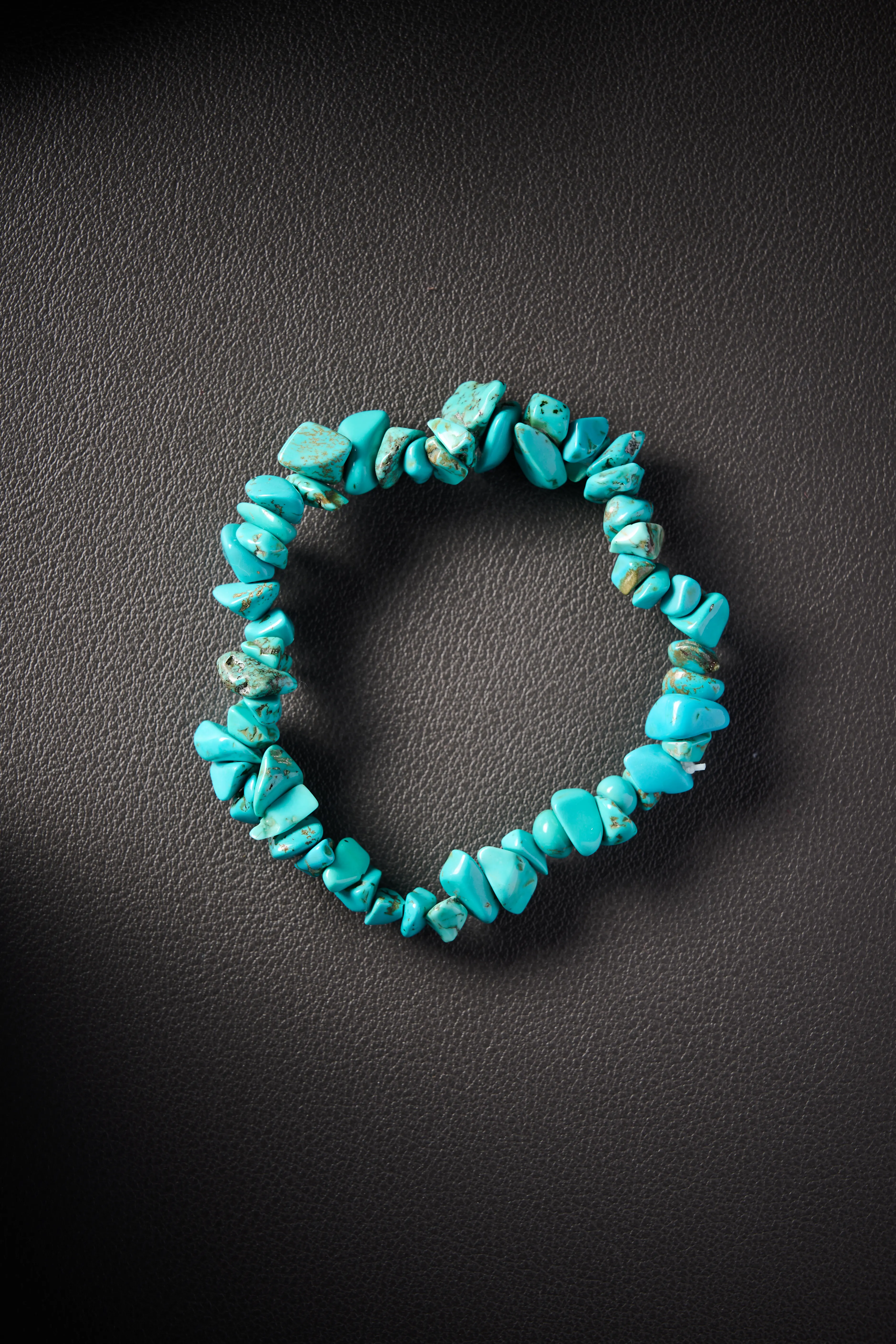 Natural turquoise crystal chip bracelet on black leather background.