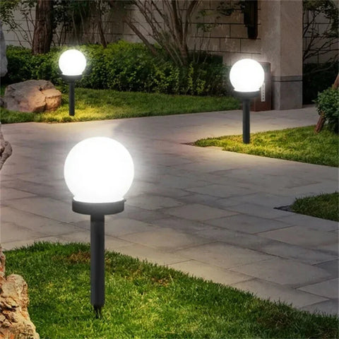 Three spherical white solar garden lights on black stakes illuminate a stone pathway and surrounding grass at night.