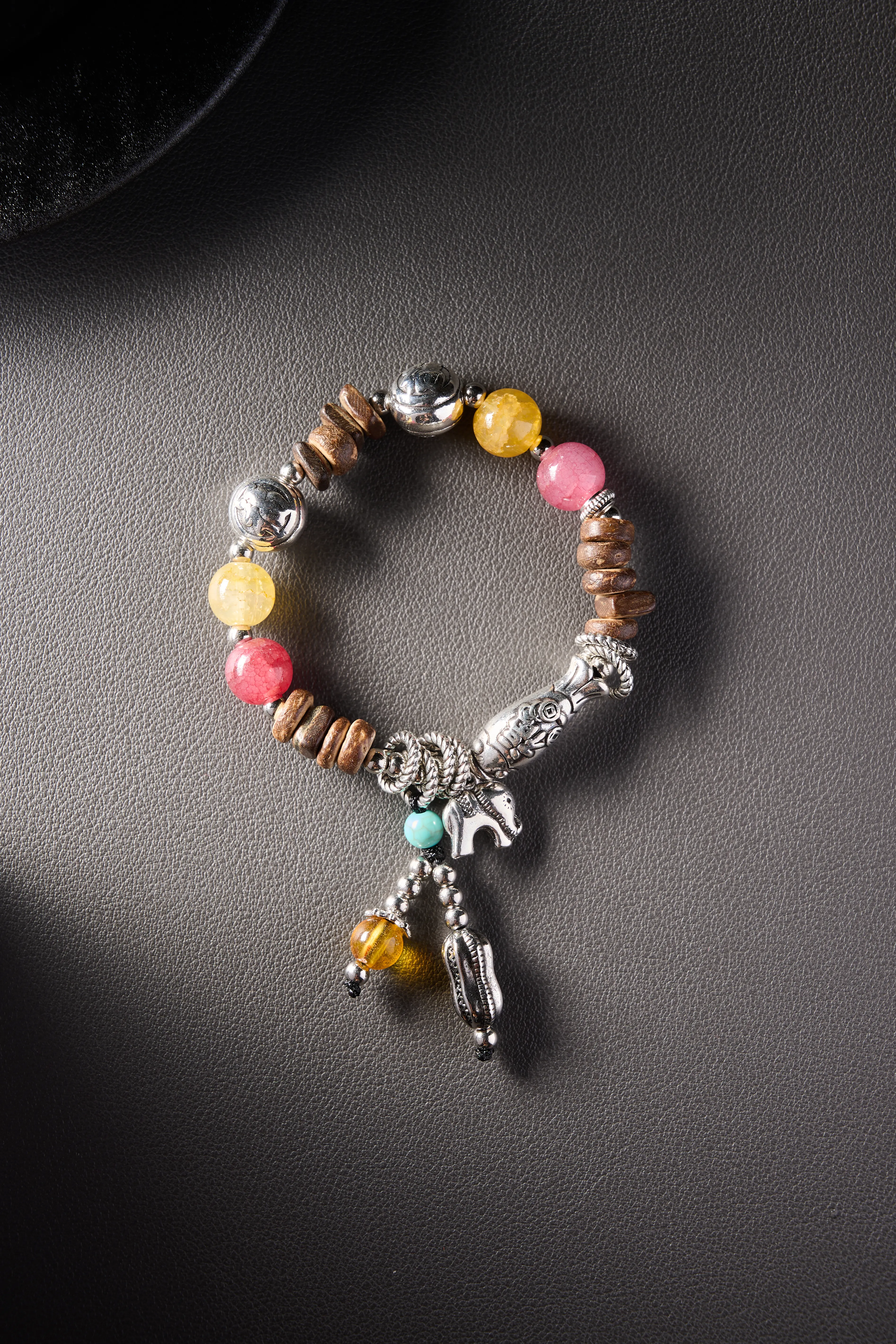 Hero image – ethnic-style bracelet with alloy charms, wooden beads, and yellow/pink natural stones on dark background.