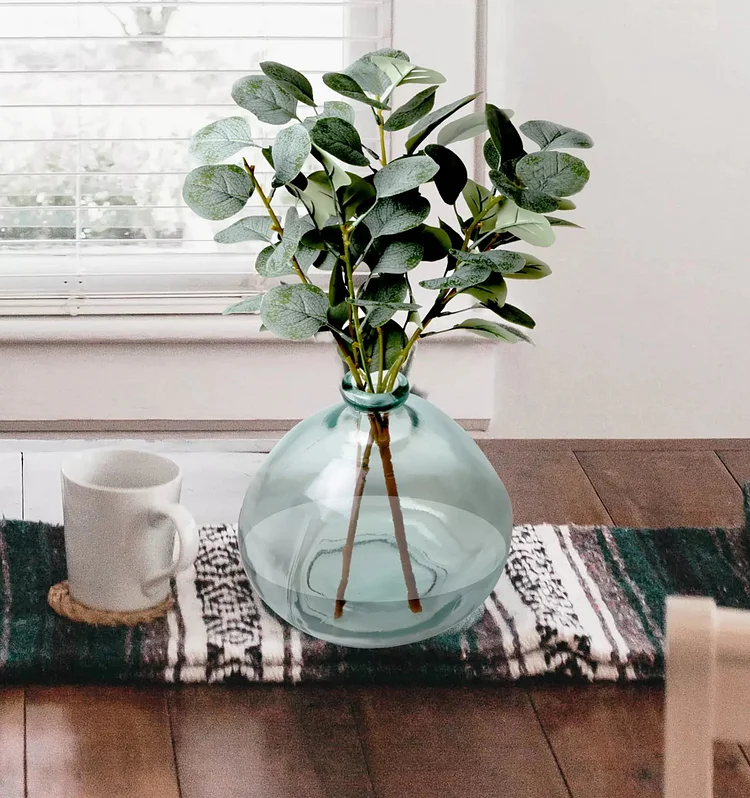 Simulated green eucalyptus adorns the glass vase, giving your home a new lease of life