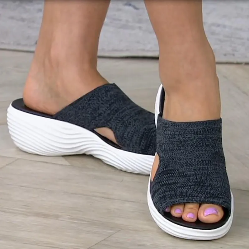 Frau trägt schwarze offene Sandalen mit gestricktem Obermaterial und dicker weißer Sohle