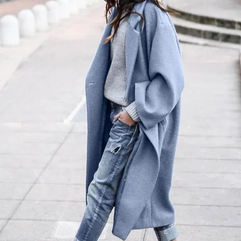 Person, die mit einem blauen, übergroßen Mantel, einem grauen Pullover und zerrissenen Jeans auf einem Bürgersteig läuft und die Hände in den Taschen hat.