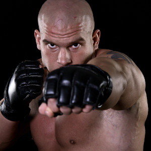 Muscular fighter, bald, shirtless wearing fingerless leather gloves, punching towards viewer