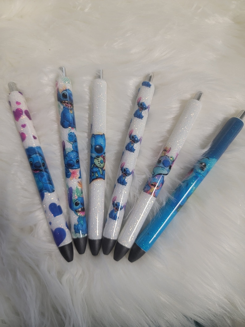 May include: Six glitter pens with blue and white designs featuring a cartoon character. The pens have black ink and silver caps.