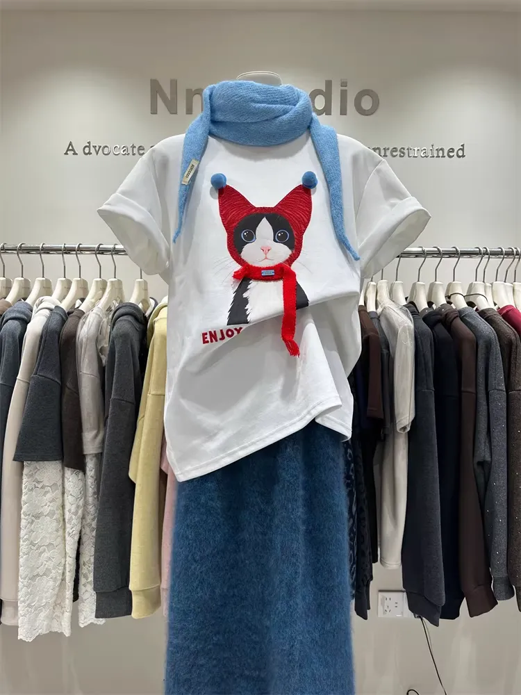 Front view of oversized white t-shirt with 3D cat wearing a red scarf and blue pom-poms