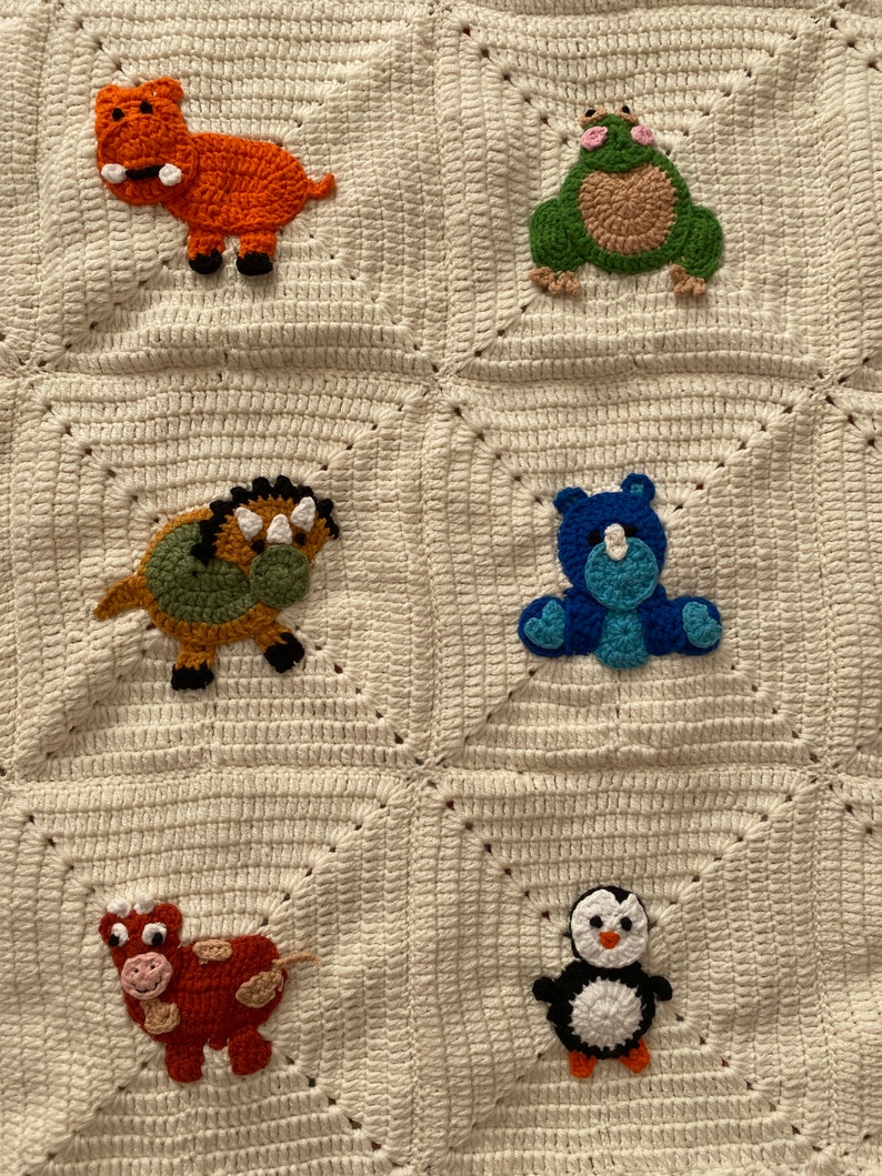 May include: A white crocheted blanket with six different animal appliques. The animals are a hippopotamus, a frog, a dinosaur, a bear, a cow, and a penguin. The animals are all different colors and have different features. The blanket is a great addition to any nursery or child's room.