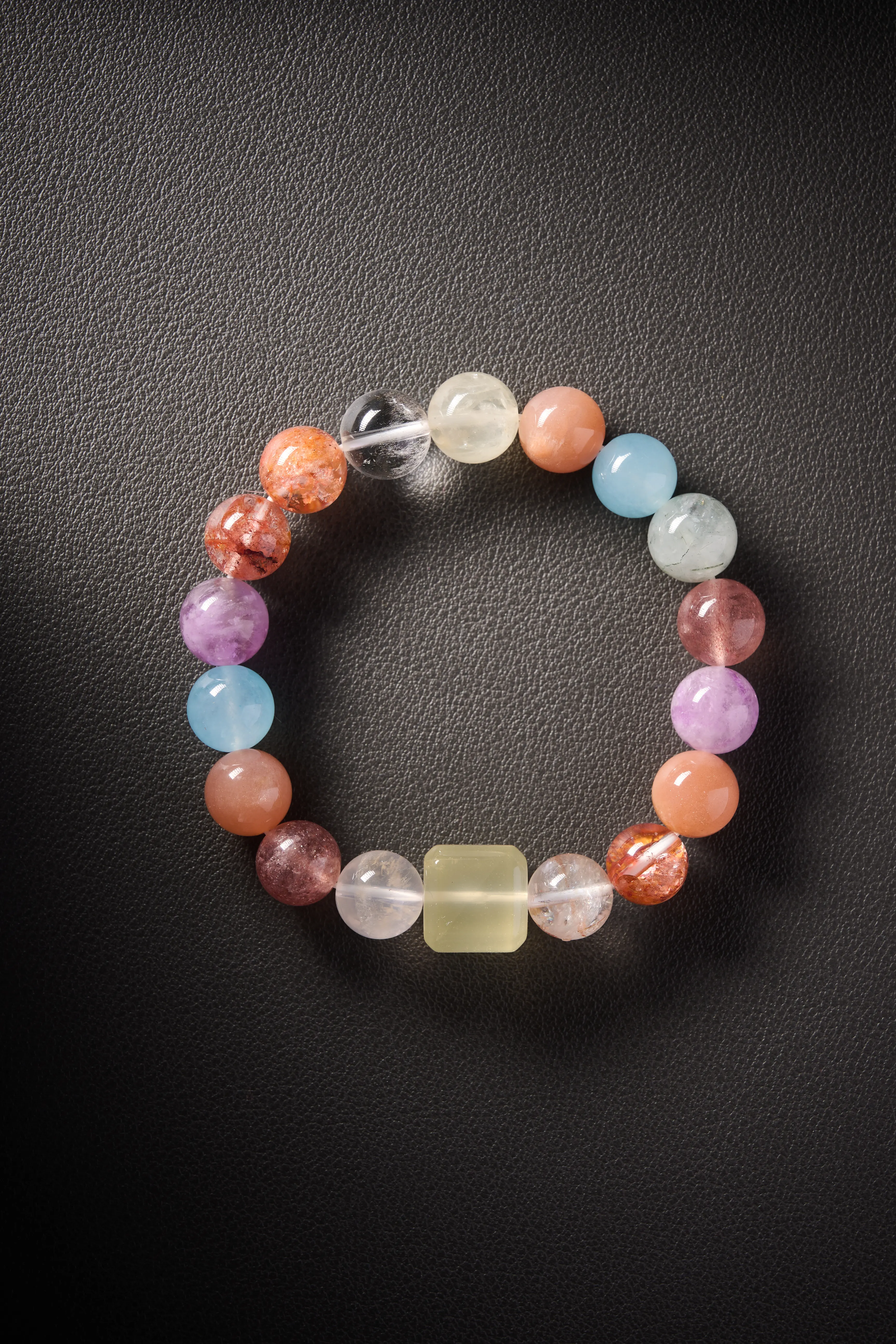 Hero image – multi-gem crystal bracelet with sunstone, aquamarine, amethyst, yellow jade and clear quartz on dark background.