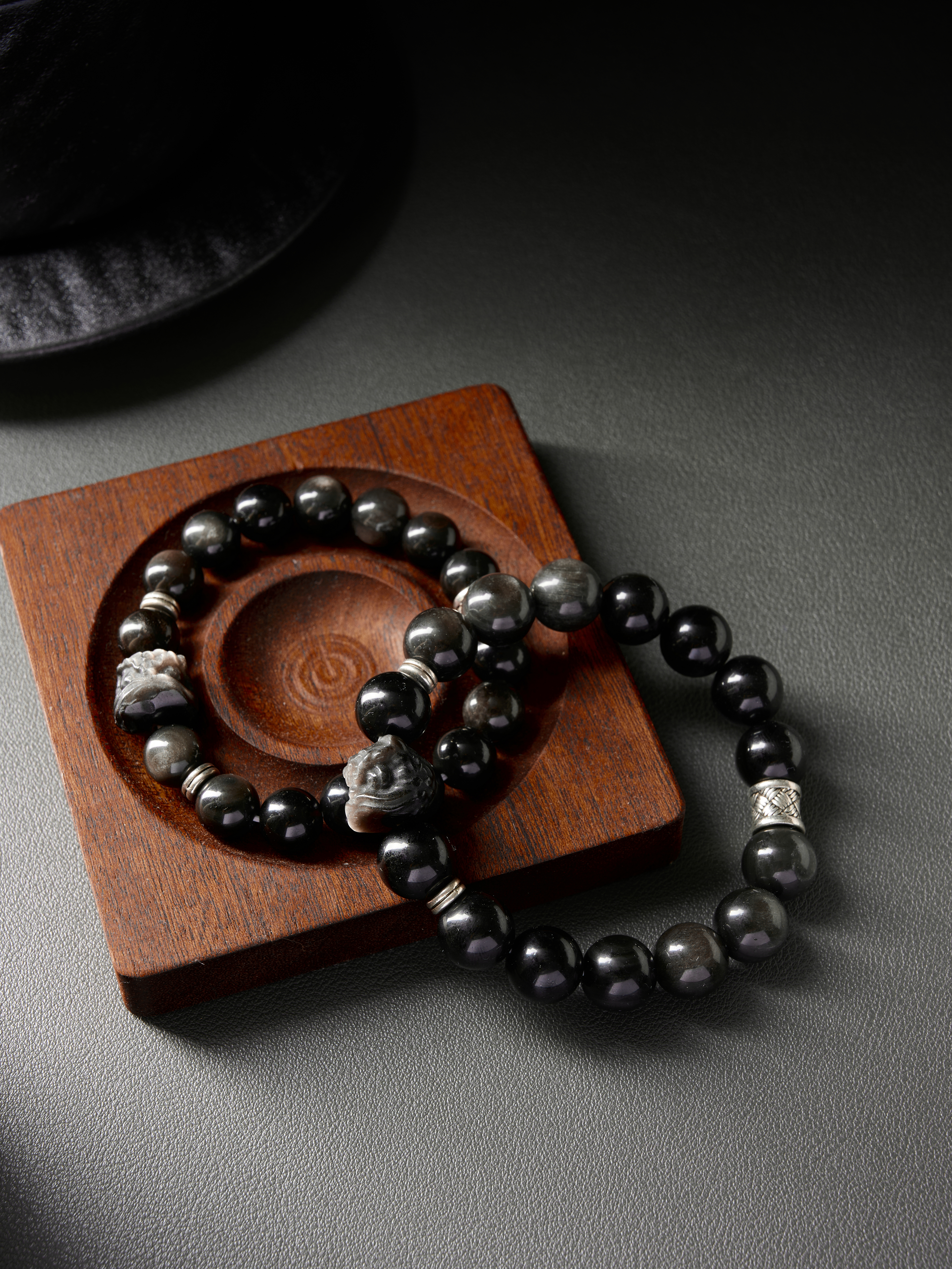 Matching obsidian bracelets side by side on neutral background, glossy black beads with vintage silver spacers