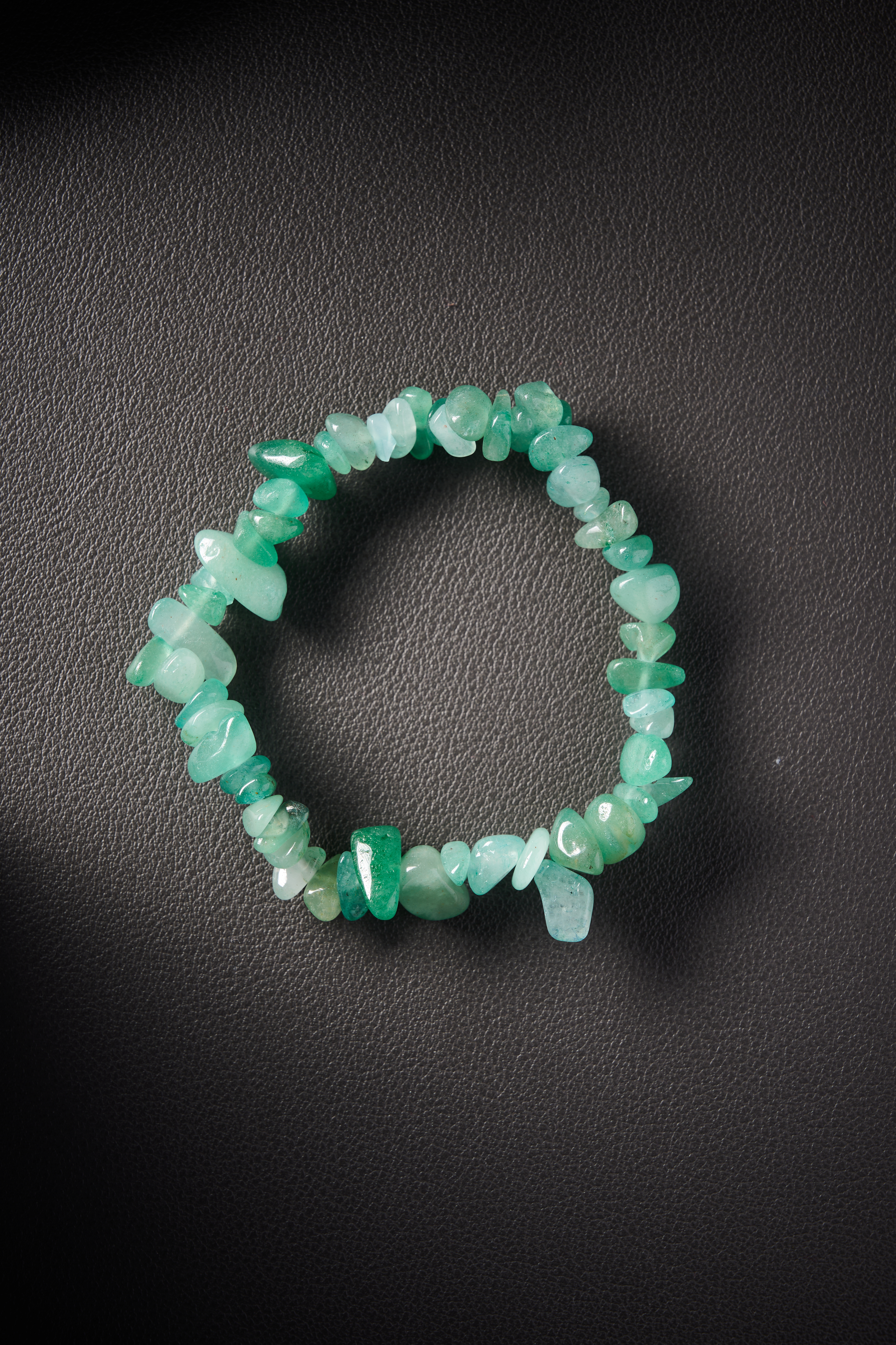 Natural green aventurine crystal chip bracelet on black leather background.