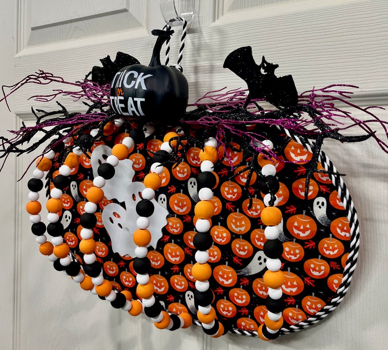 可能包含:黑白万圣节花环,搭配黑白串珠花环。花环上装饰着橙色和黑色的南瓜、白色幽灵和一只黑色蝙蝠。花环边缘为黑白条纹,黑色背景上印有白色“Trick or Treat”(不给糖就捣蛋)字样。