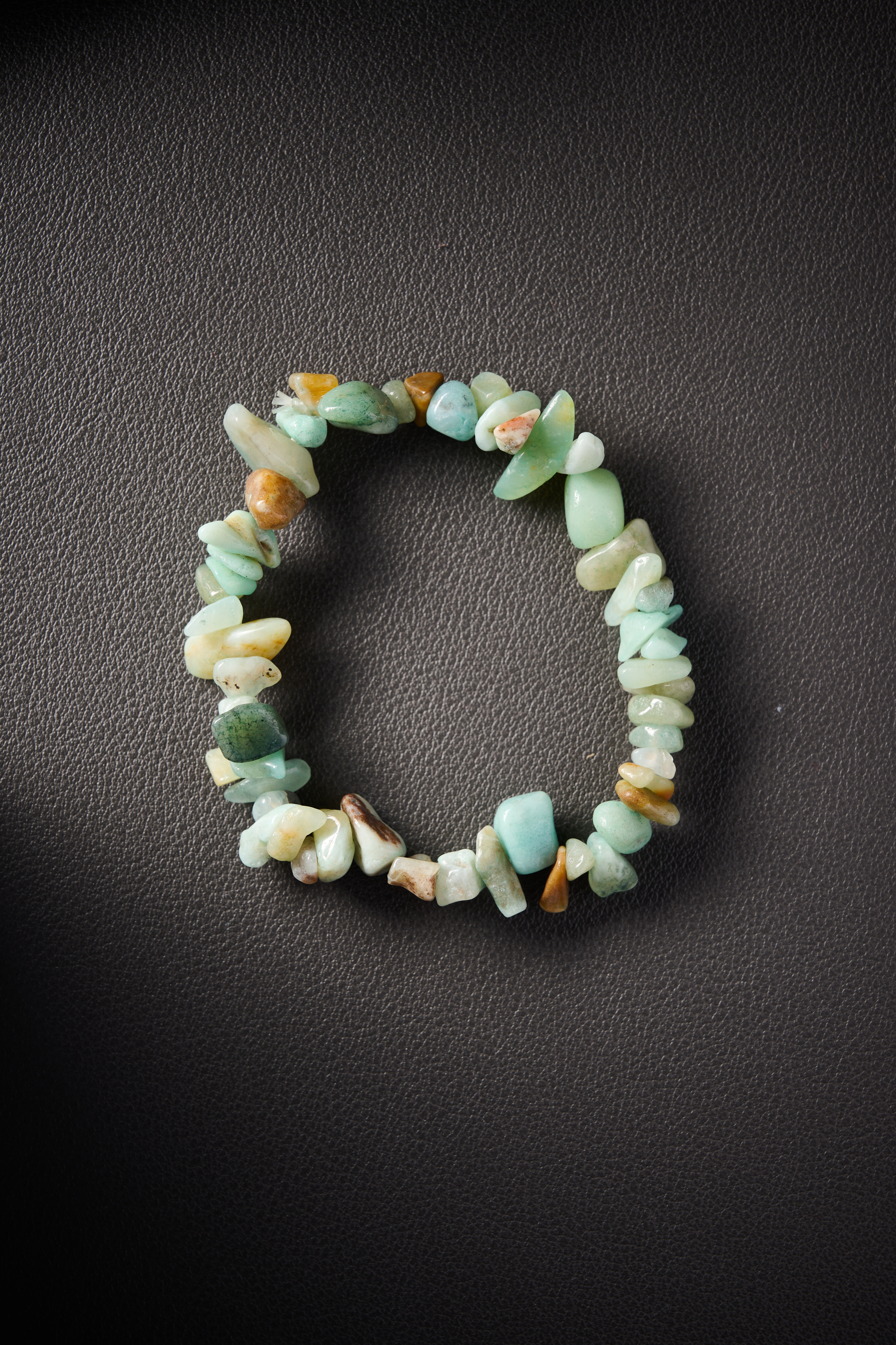 Natural prehnite crystal chip bracelet on black leather background.