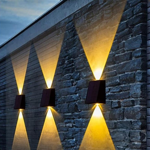 Three small, dark, rectangular lights are mounted on a brick wall, casting a warm white downward glow.