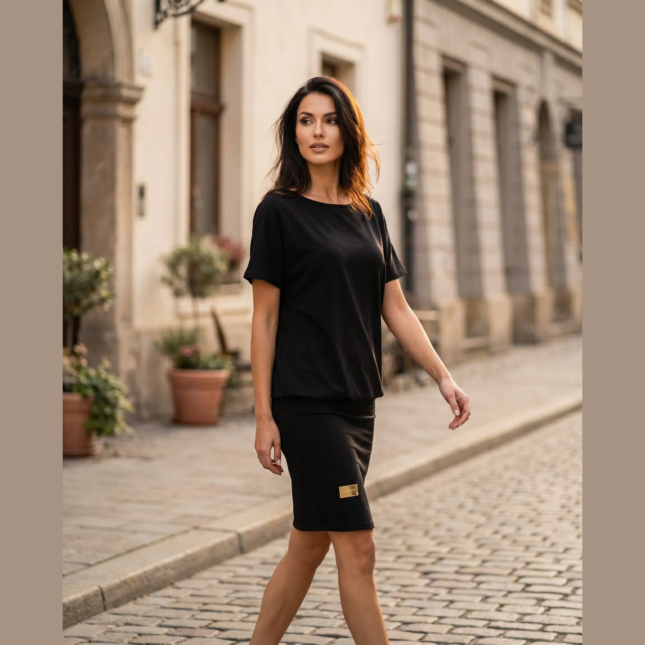 Woman wearing the black Melissa relaxed stretch dress, walking on a sunlit street