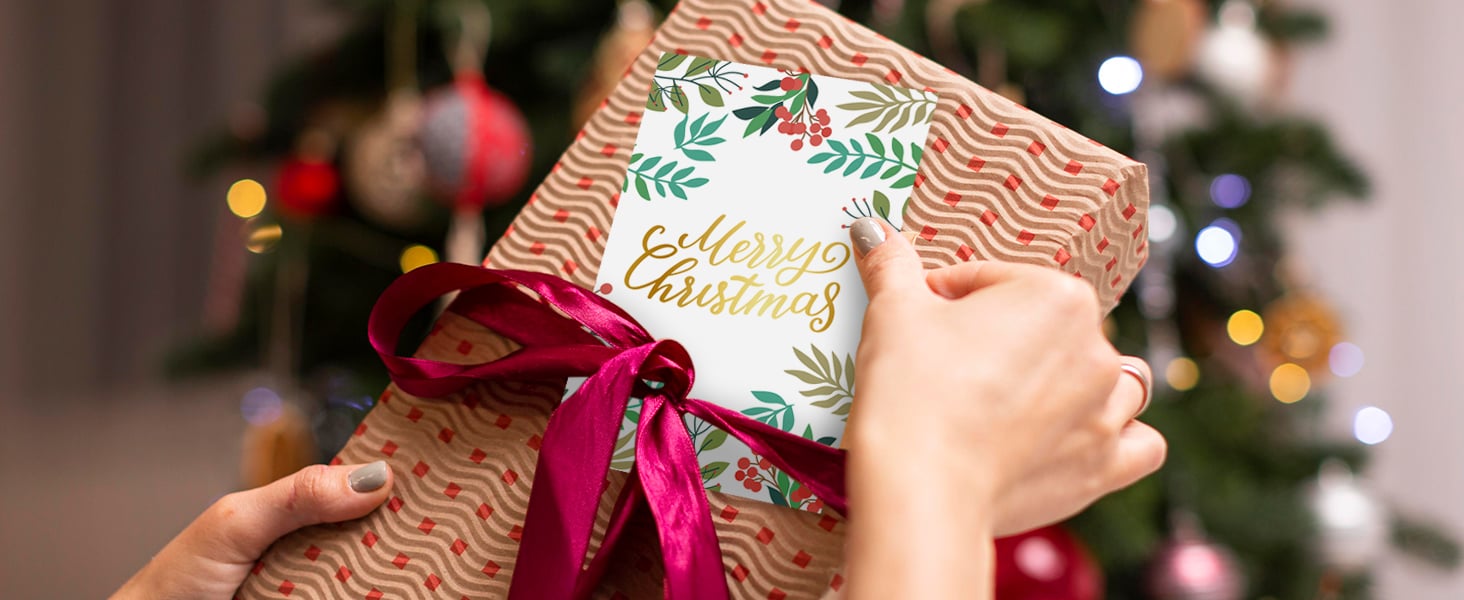 A gift a ribbon together with a christmas card assorted with a chrismas tree background is shown.