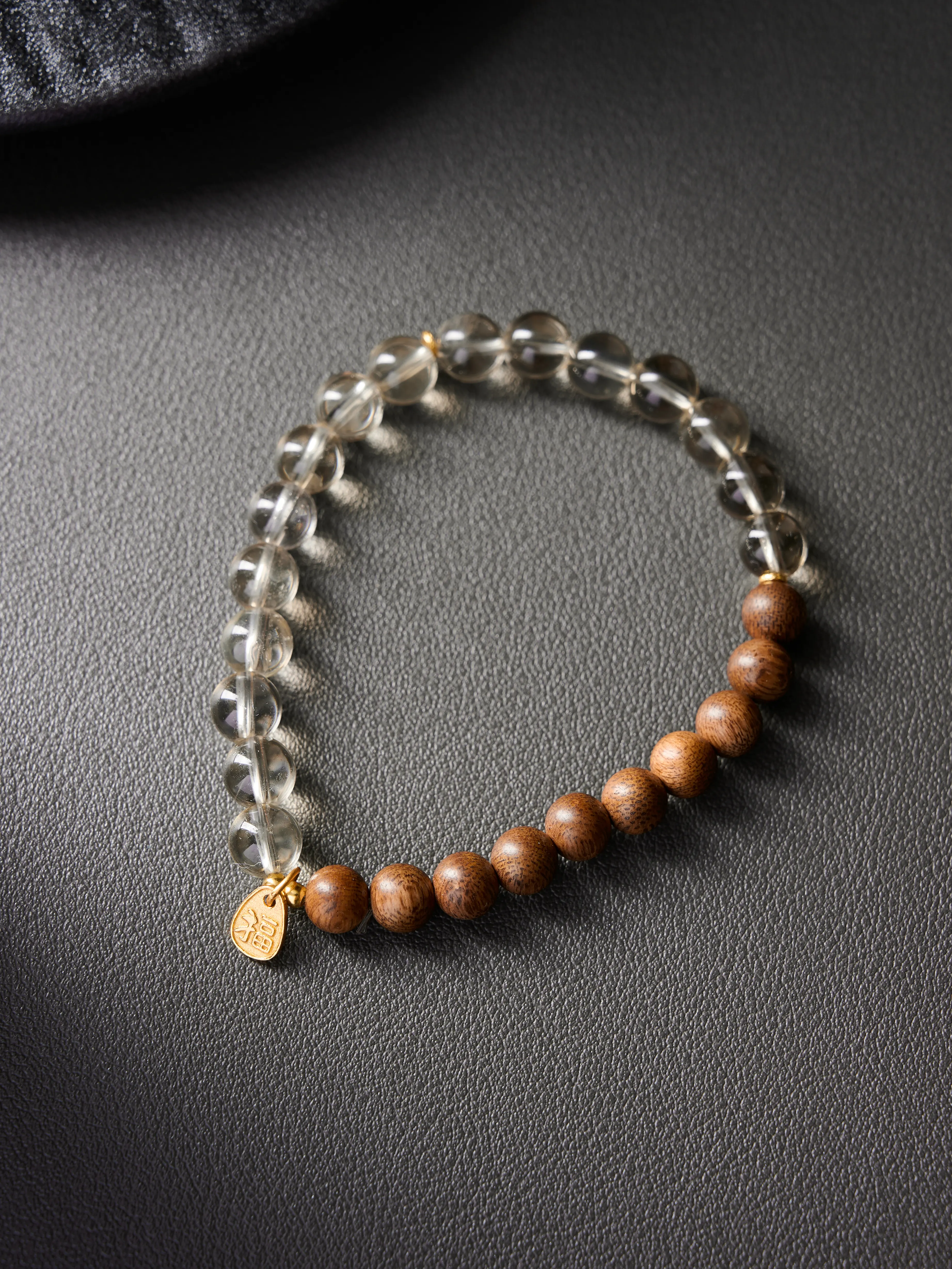 Flat lay on wooden block showing natural sandalwood grain beads paired with clear crystal
