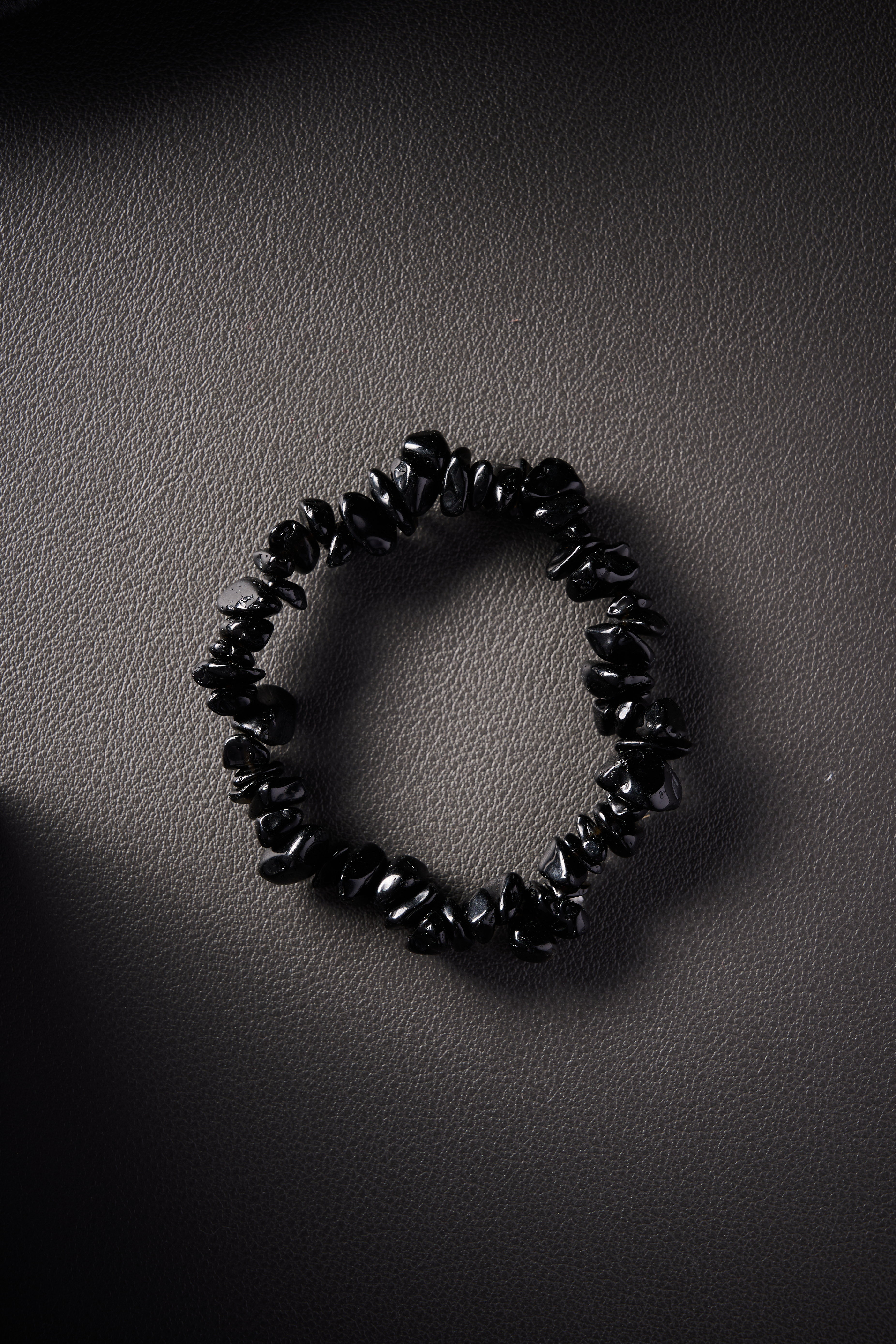 Natural obsidian crystal chip bracelet on black leather background.