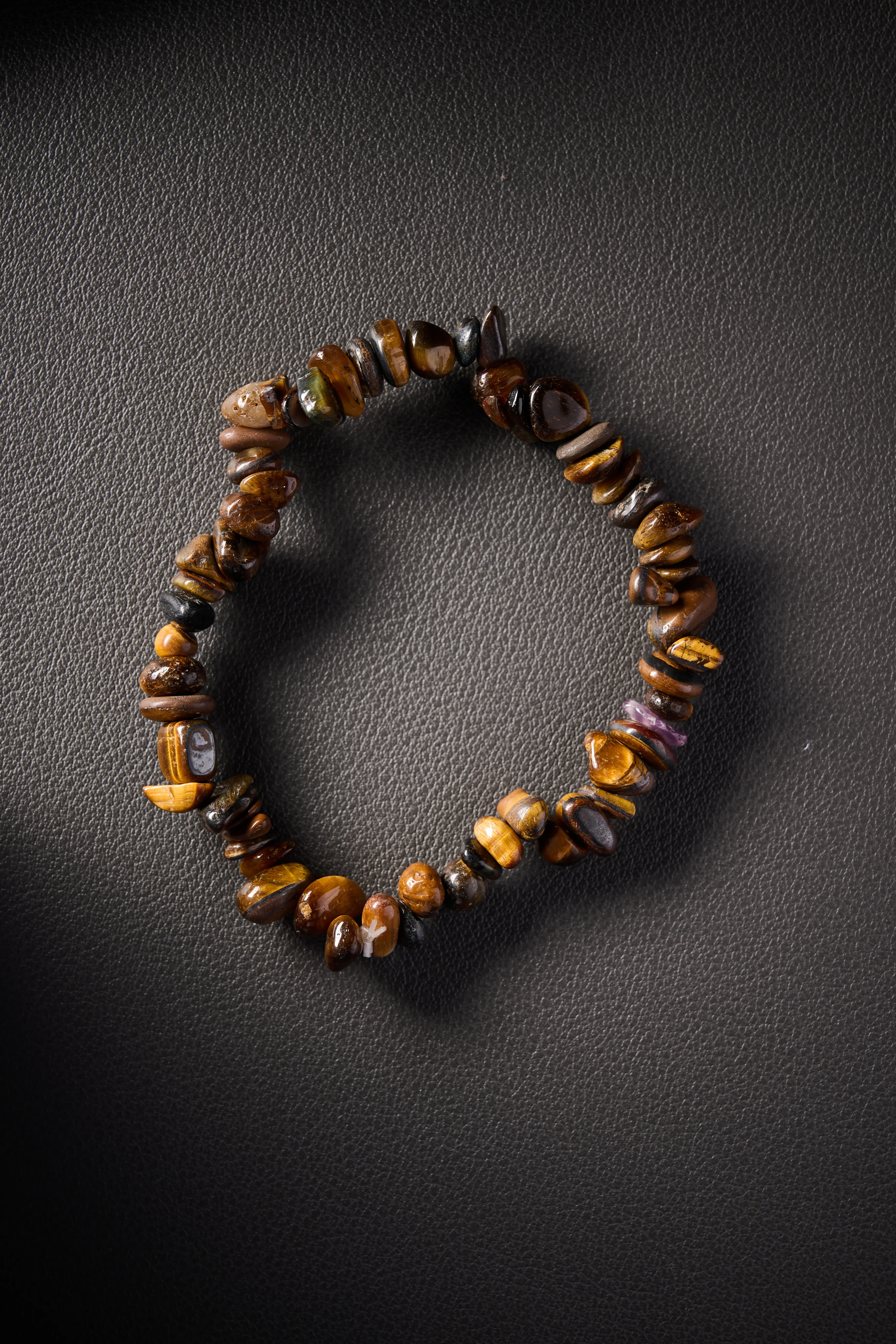Natural tiger’s eye crystal chip bracelet on black leather background.