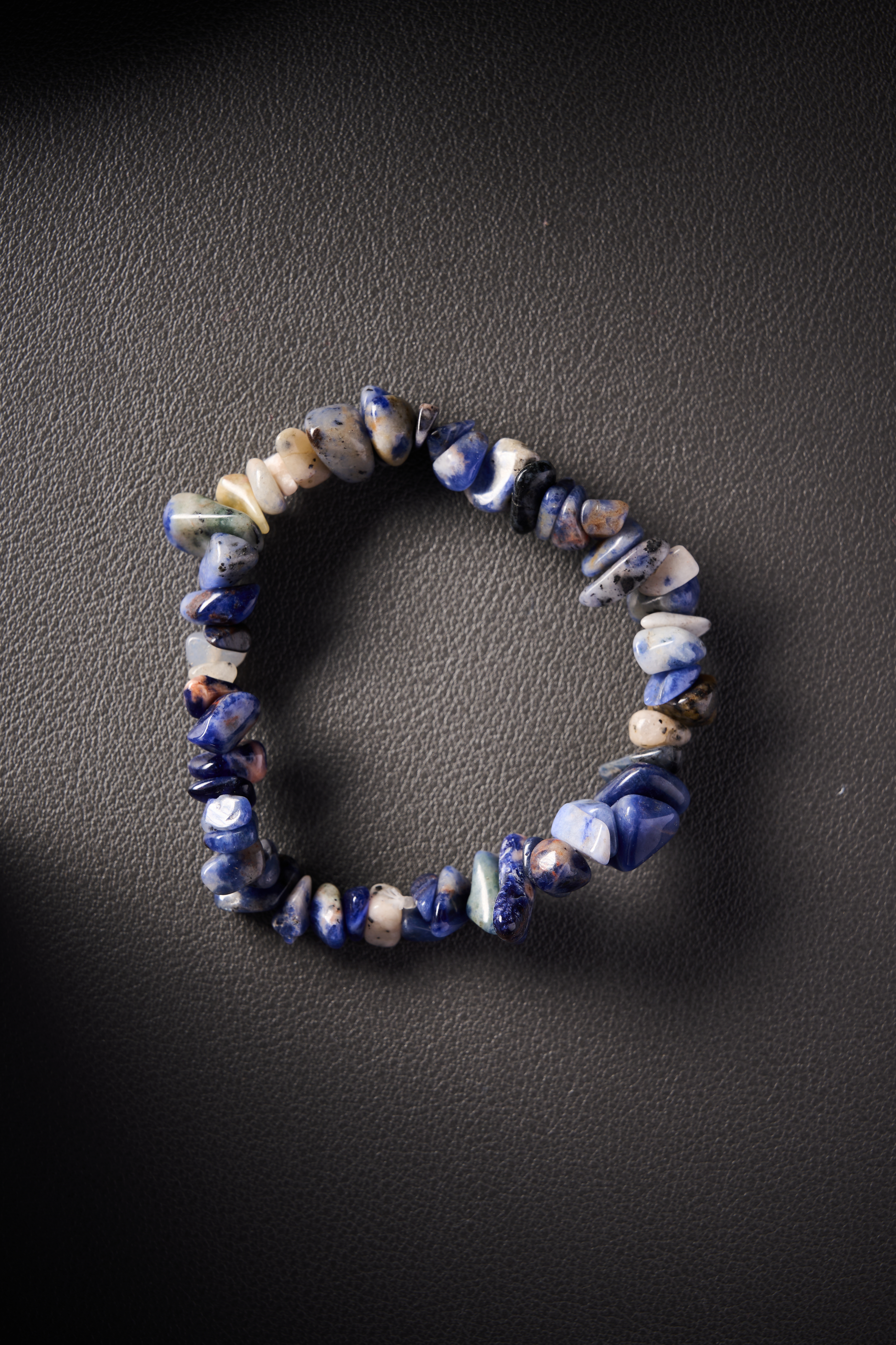 Natural blue sodalite crystal chip bracelet on black leather background.