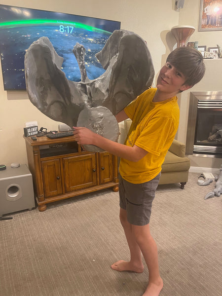 男孩手持巨型3D打印霸王龙骨架组件向众人展示