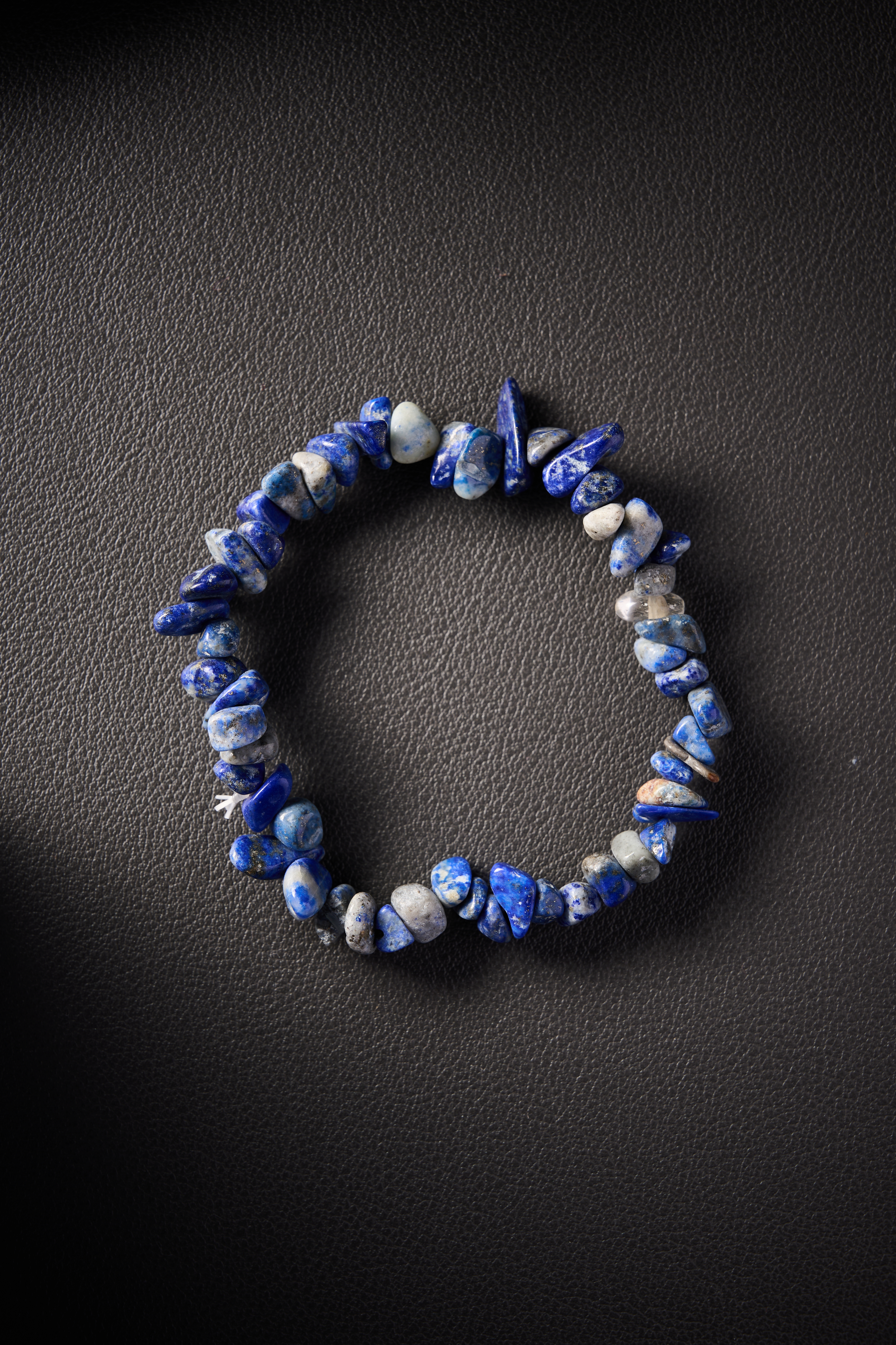 Natural lapis lazuli crystal chip bracelet on black leather background.