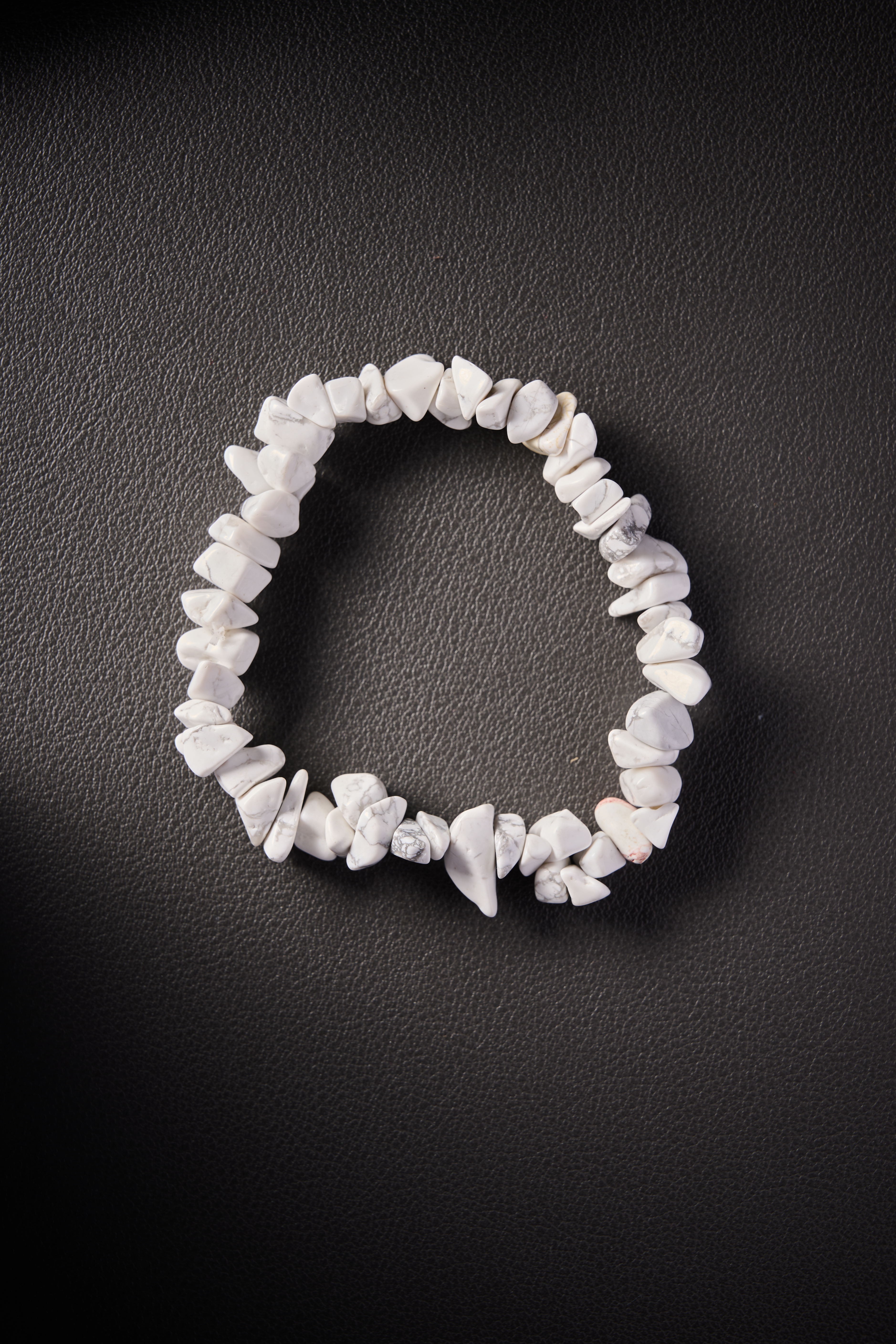 Natural Howlite crystal chip bracelet on dark leather background.