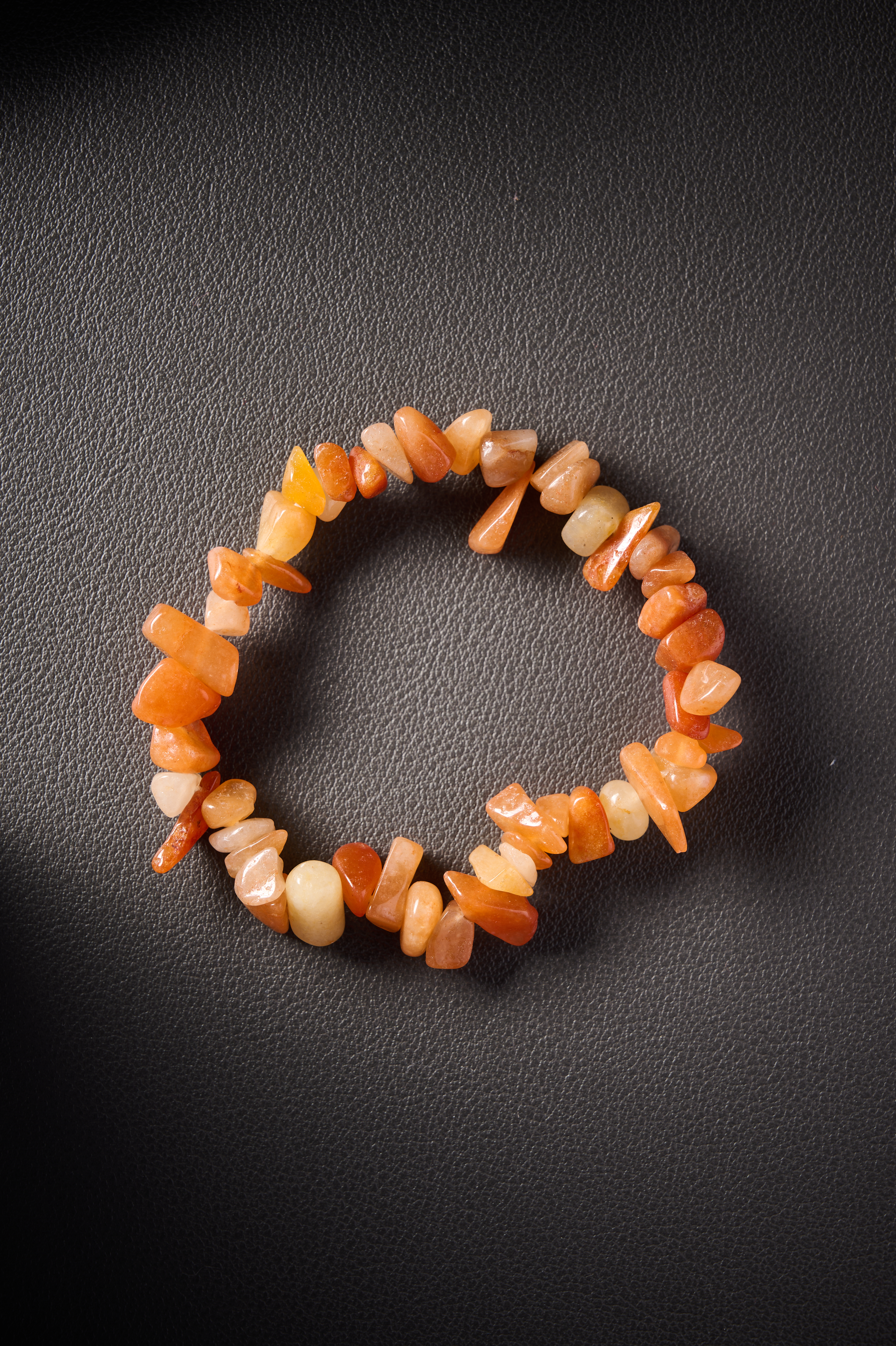 Natural orange agate crystal chip bracelet on black leather background.