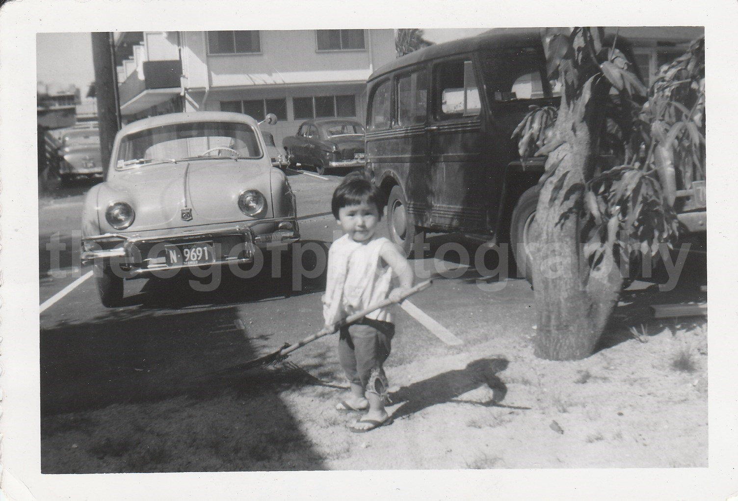 A LITTLE GIRL WITH A RAKE Found Photo Poster painting bwClassic Cars VINTAGE 7614