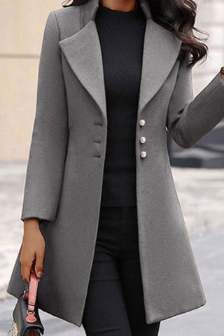 Eine Frau trägt einen eleganten schwarzen Mantel, dazu ein Grau Oberteil und eine schwarze Hose