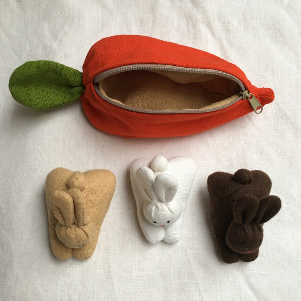 A carrot purse bursting with three multicultural bunnies