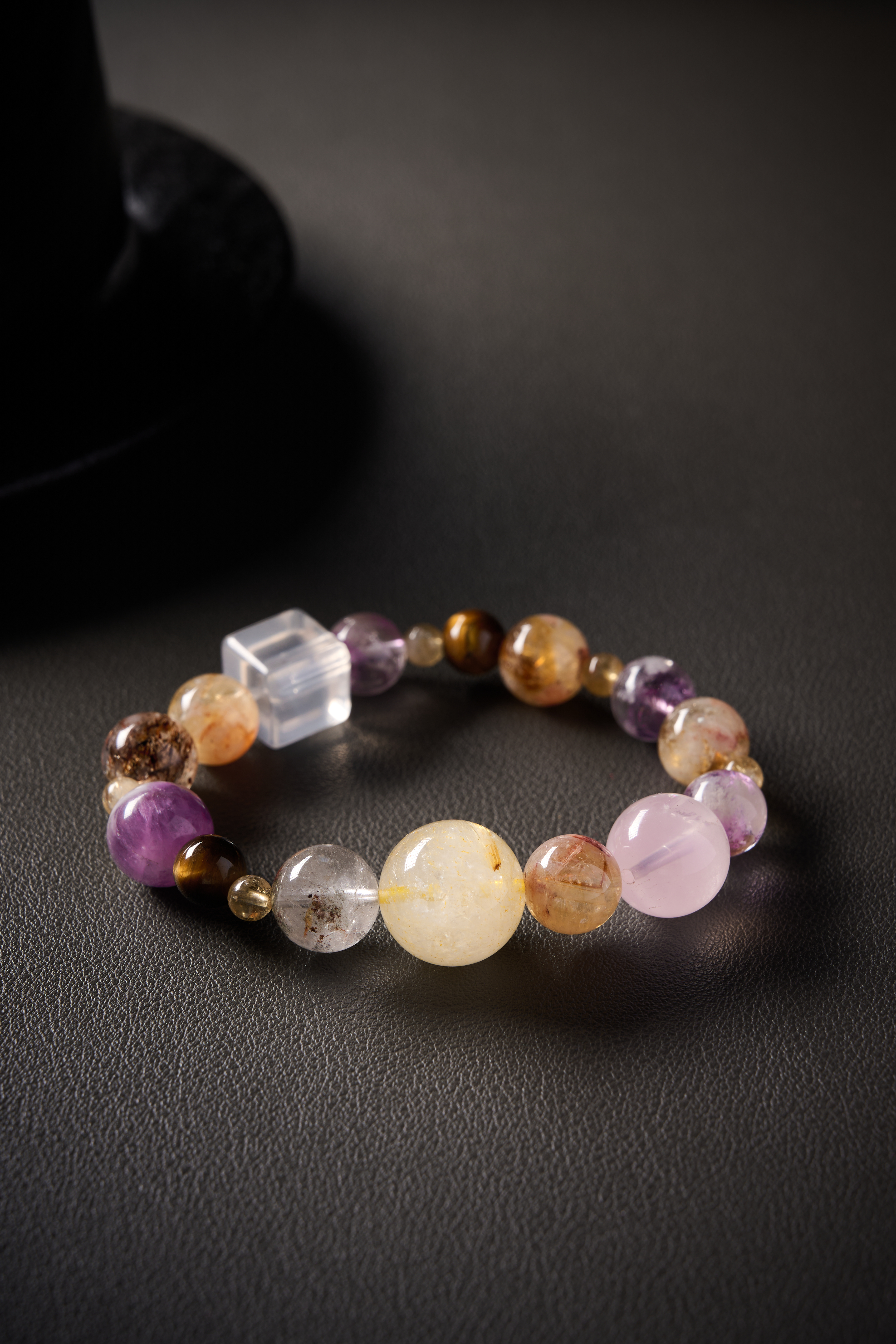 Close-up of gemstone mix – polished round beads showing rutile threads, amethyst purple and citrine golden tones, high gloss.