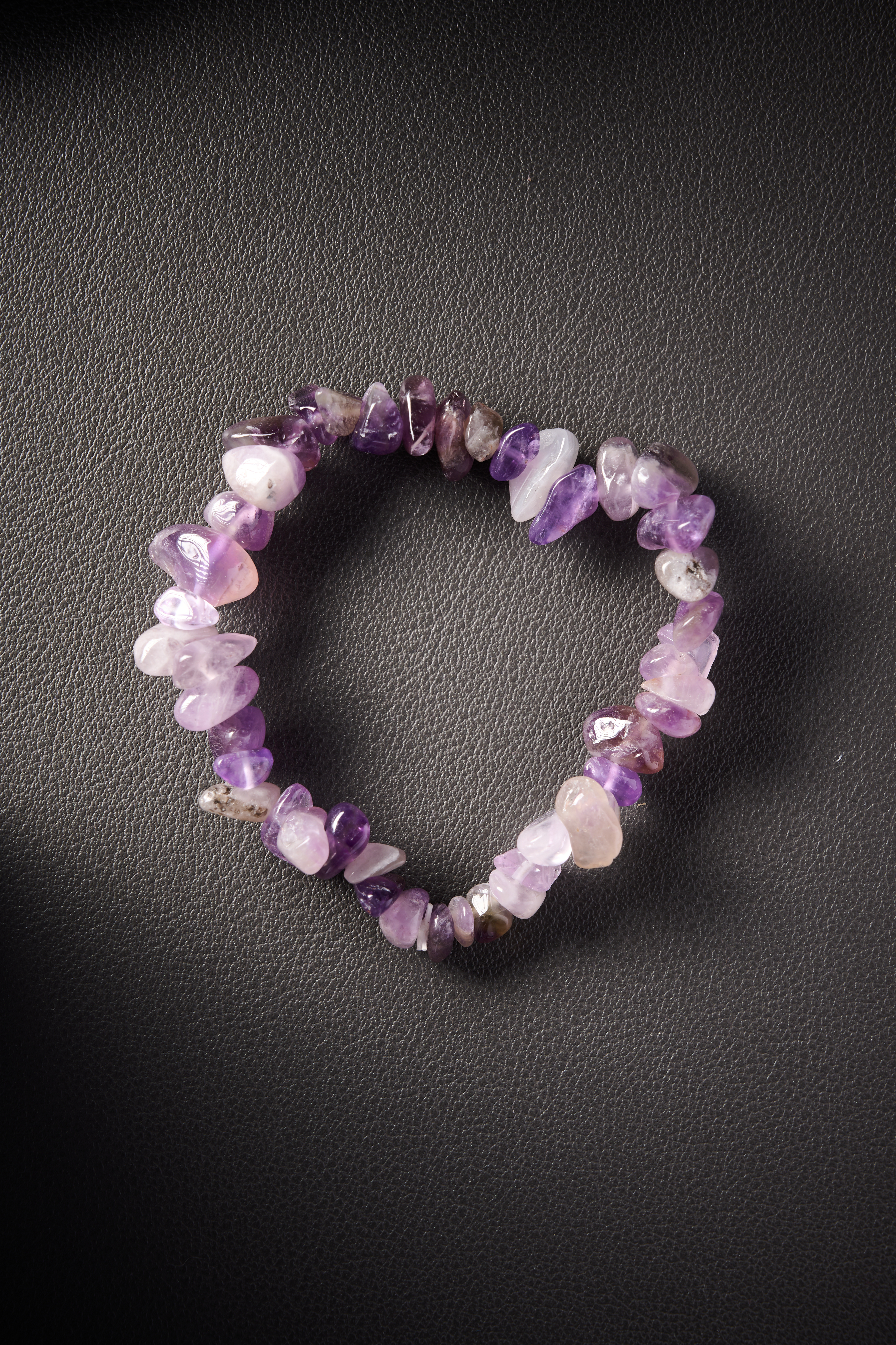 Natural amethyst crystal chip bracelet on black leather background.