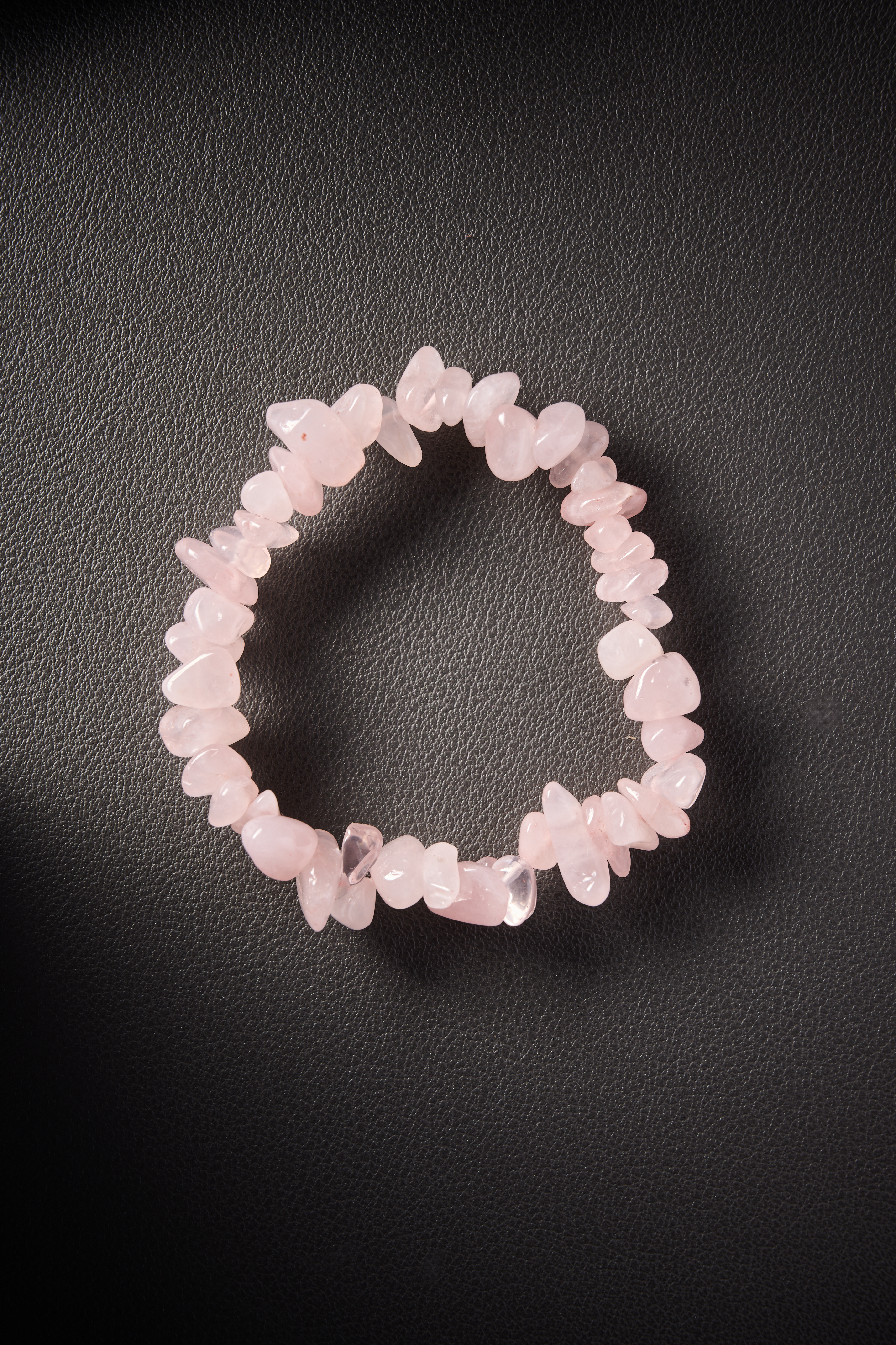 Natural rose quartz crystal chip bracelet on dark leather background.