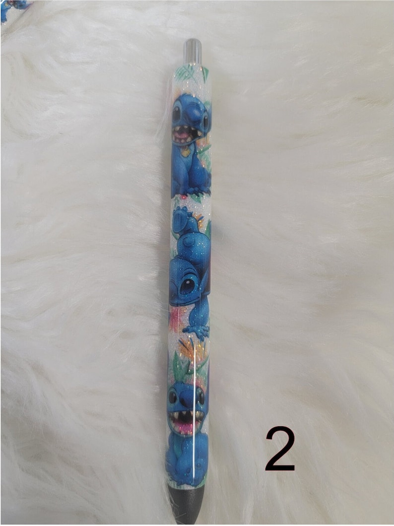 May include: A white pen with a blue glitter finish and a design of blue cartoon characters with a floral pattern. The number 2 is written in black on the white background.