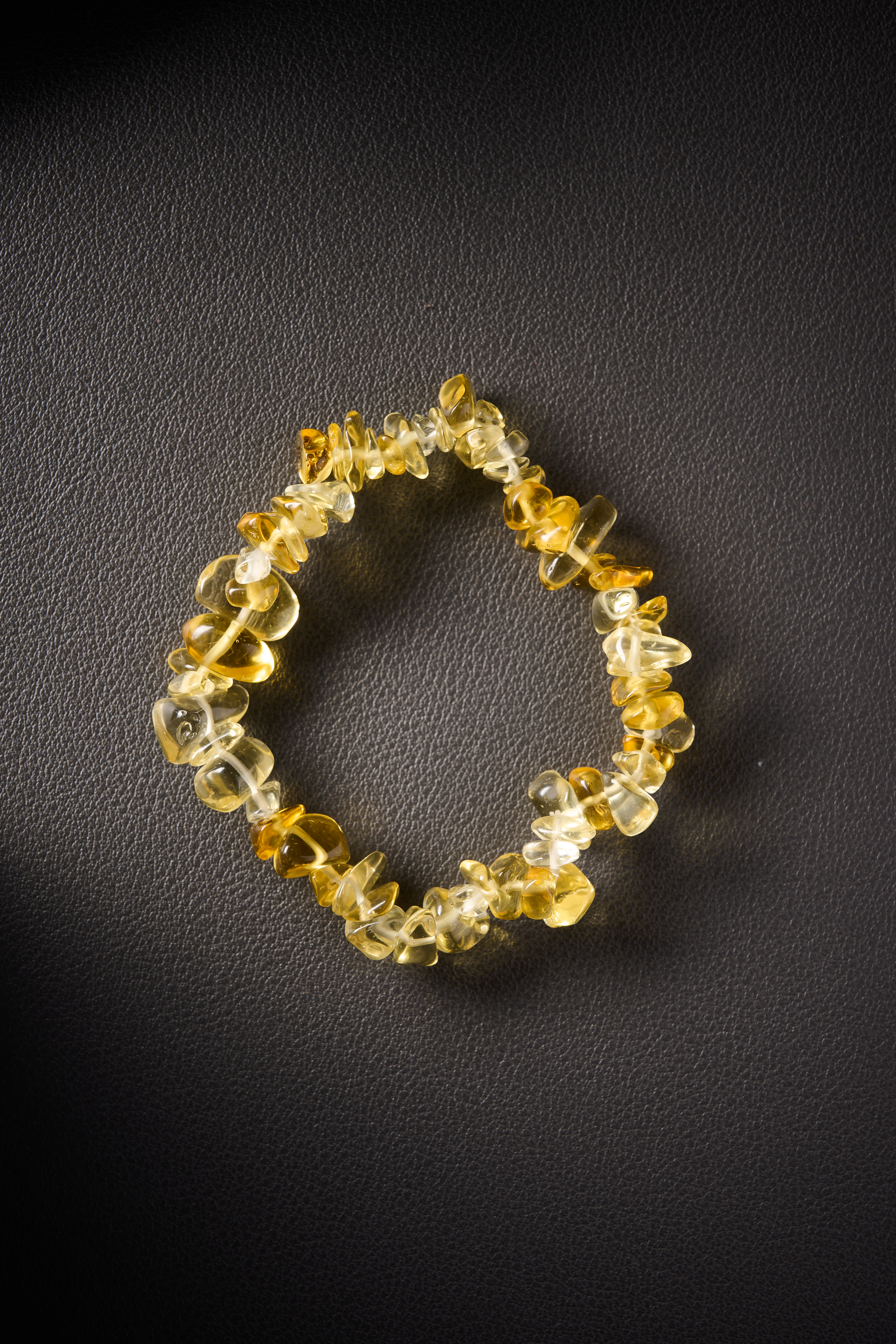 Natural yellow jade crystal chip bracelet on black leather background.