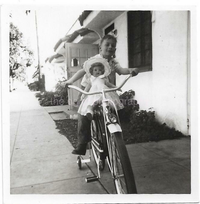 A Girl And Her Doll Riding A Bicycle With Training Wheels bw FOUND Photo Poster painting D 02 9