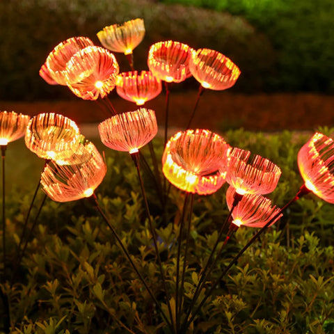 Numerous solar-powered garden lights with a jellyfish-like appearance emit a warm orange glow in a garden at night, standing above dark green foliage.