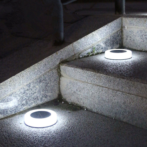 Two round, white solar pathway lights with dark centers are embedded in stone steps at night, emitting a bright white upward glow.