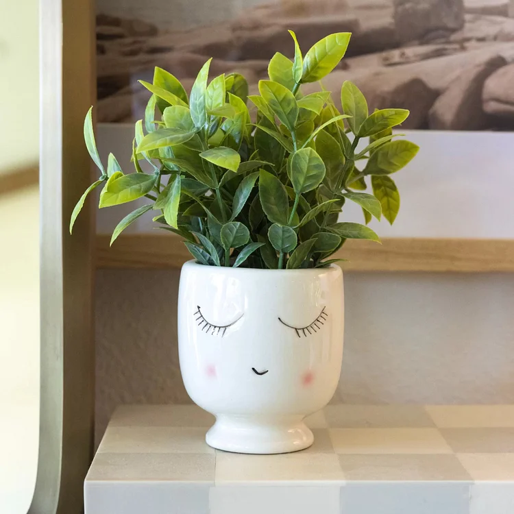 A shy porcelain girl holds her in her arms, and simulated tea plants surround the table