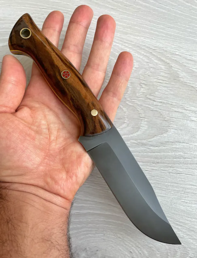 Cuțit Bowie cu lamă din oțel carbon 1075, m&acirc;ner din nuc cu finisaj lustruit, construcție full-tang și teacă din piele.