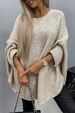Eine Frau trÃ¤gt einen lockeren, Ã¼bergroÃŸen beigen Strickpullover mit langen Ã„rmeln und rundem Ausschnitt, dazu eine Uhr und eine Handtasche.